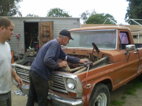 1969 Ford F-250 - Two men work on the engine of an orange 1967 Ford F-100 pickup truck.
