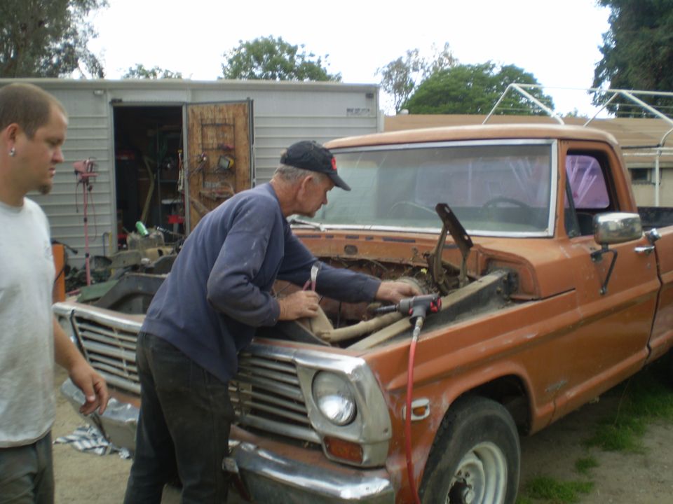 Orange 1967 Ford F-100 pickup truck with hood open, men working on engine
