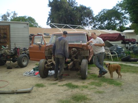 1969 Ford F-250 - Two men and a dog stand around a disassembled orange Ford F-Series truck in a yard.