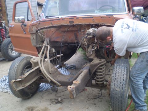 1969 Ford F-250 - A man works on the engine of an orange 1969 Ford F-250 truck chassis, with the front end disassembled.