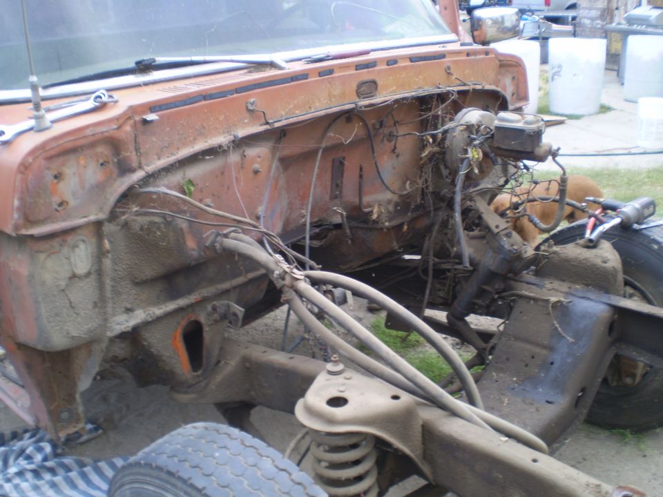 Disassembled truck engine bay, showing frame and suspension components. A dog is visible in the background