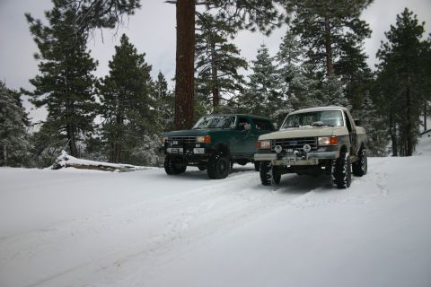 1991 Ford Bronco - Two trucks are parked in a snowy forest, ready for off-road adventure.