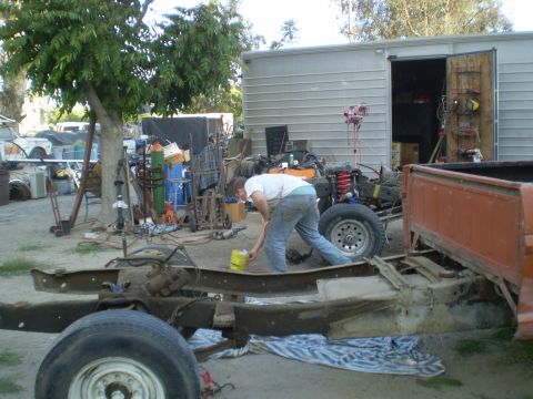 1969 Ford F-250 - A person cleans the frame of a truck with an orange bed in a cluttered yard.