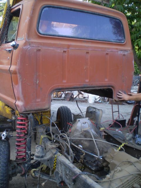 1969 Ford F-250 - The side view of an orange pickup truck cab and chassis, with the bed removed and the frame exposed, is shown during a repair process.