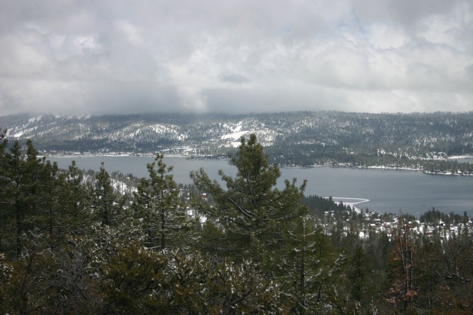 Snowy mountains and trees overlook a lake with a cloudy sky