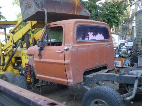 1969 Ford F-250 - A Ford truck cab is suspended by chains from a loader, with the chassis and rear wheels visible below.