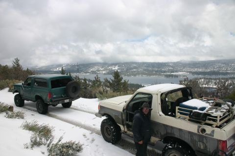 1991 Ford Bronco - Two trucks are parked on a snowy road overlooking a lake and mountains.