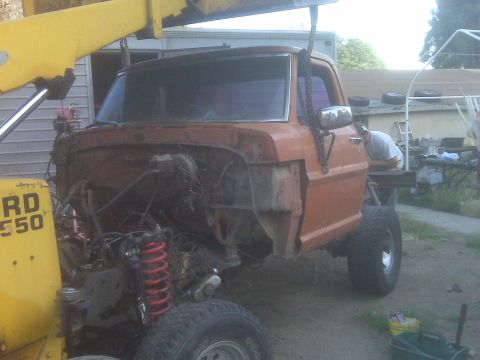 1969 Ford F-250 - The cab of a 1969 Ford F-250 pickup truck is suspended by a yellow crane, revealing its disassembled front end.