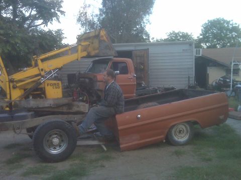 1969 Ford F-250 - Ford F-series truck chassis and a Ford backhoe loader are parked outdoors. A man is sitting on the truck bed.