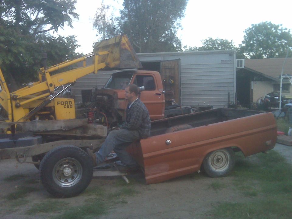 Ford F-series truck chassis with a backhoe loader next to it. A man sits on the truck bed