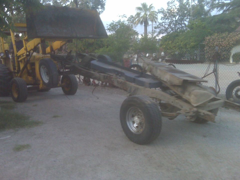 Truck chassis with fuel tank, being lifted by a yellow loader