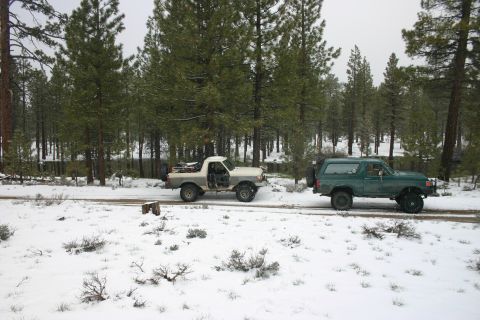 1991 Ford Bronco - Two SUVs drive on a dirt road through a snow-covered forest.