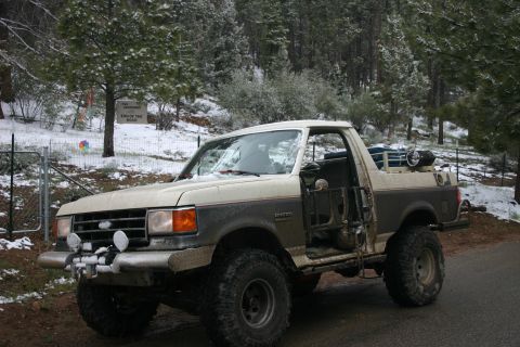 1991 Ford Bronco - This modified Ford Bronco is parked on a snowy, wooded road. A sign in the background reads 'End of the Road'.