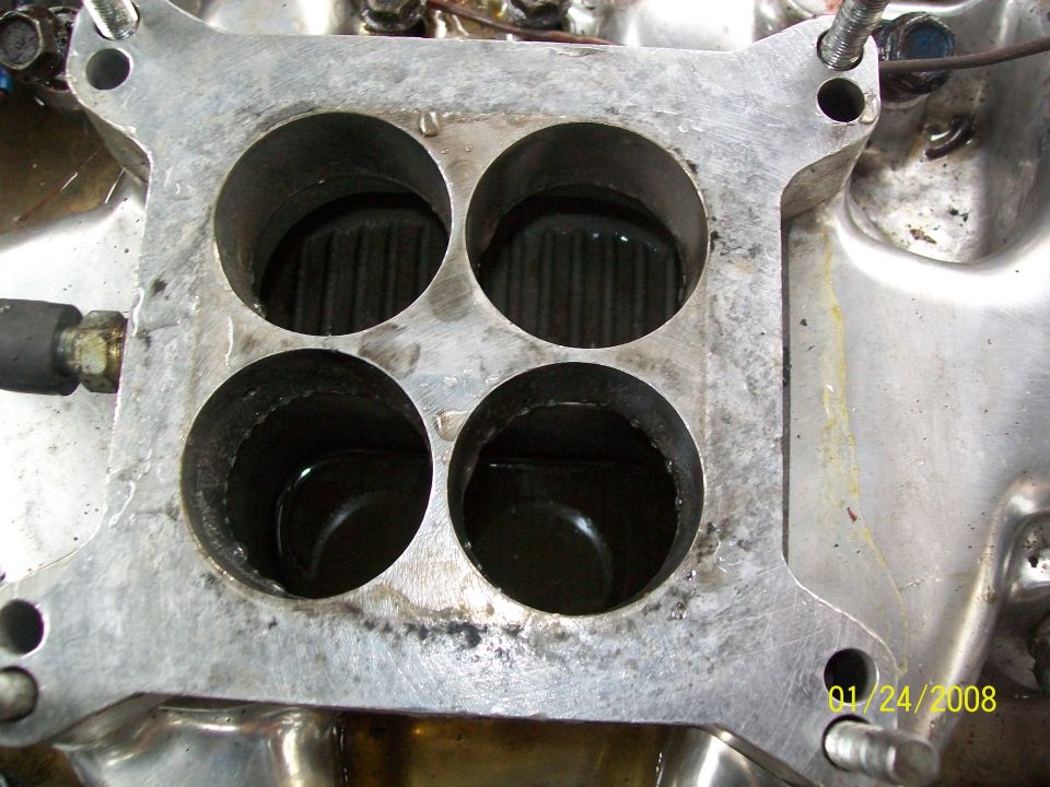 Close-up of a four-barrel carburetor intake manifold with visible oil and grime