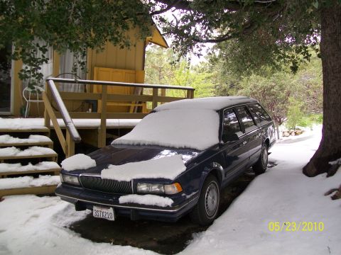 1972 Ford Ranchero - A dark blue station wagon sits covered in snow next to a wooden cabin on a snowy day.