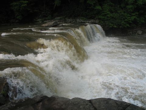 1985 Ford Bronco - A powerful waterfall flows over rocks, surrounded by lush green trees.