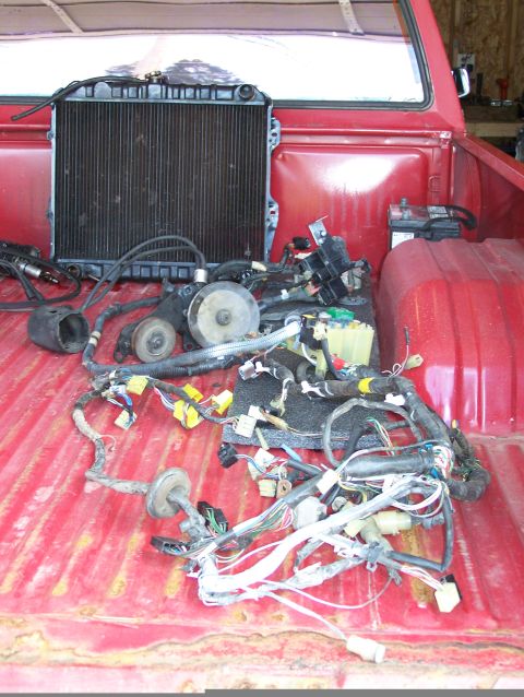 1988 Suzuki Samurai - Radiator and wiring harness are piled in the bed of a red truck.