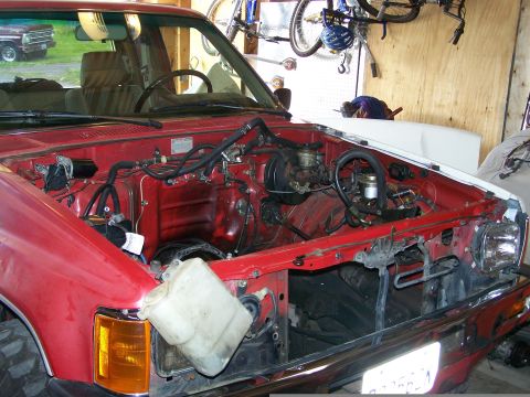 1988 Suzuki Samurai - The engine bay of a red pickup truck is shown, with the hood open and some components removed. Another vehicle is visible outside.