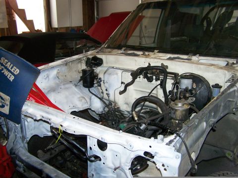 1988 Suzuki Samurai - The engine bay of a white truck is visible, with a blue container to the left and another vehicle in the background.