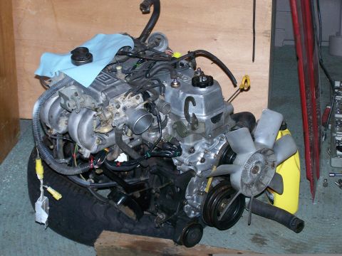 1988 Suzuki Samurai - Engine assembly resting on a tire, with various components attached.