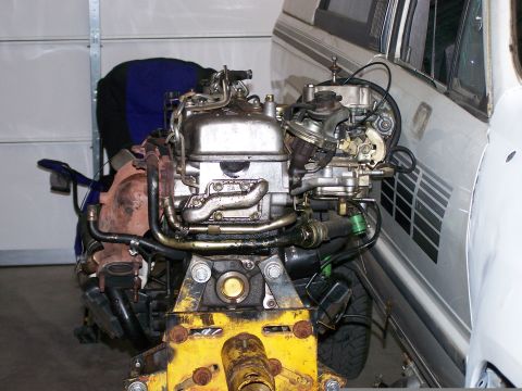 1988 Suzuki Samurai - An engine is mounted on a stand in front of a white vehicle, possibly in a garage.