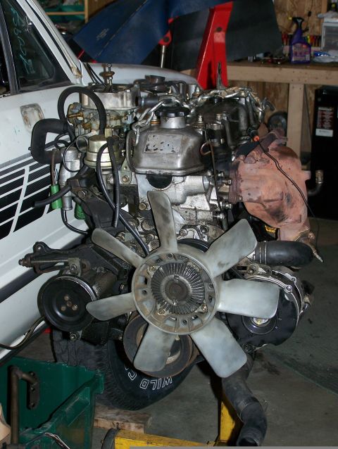 1988 Suzuki Samurai - Engine assembly with visible fan, belts, and hoses, partially installed in a white vehicle.