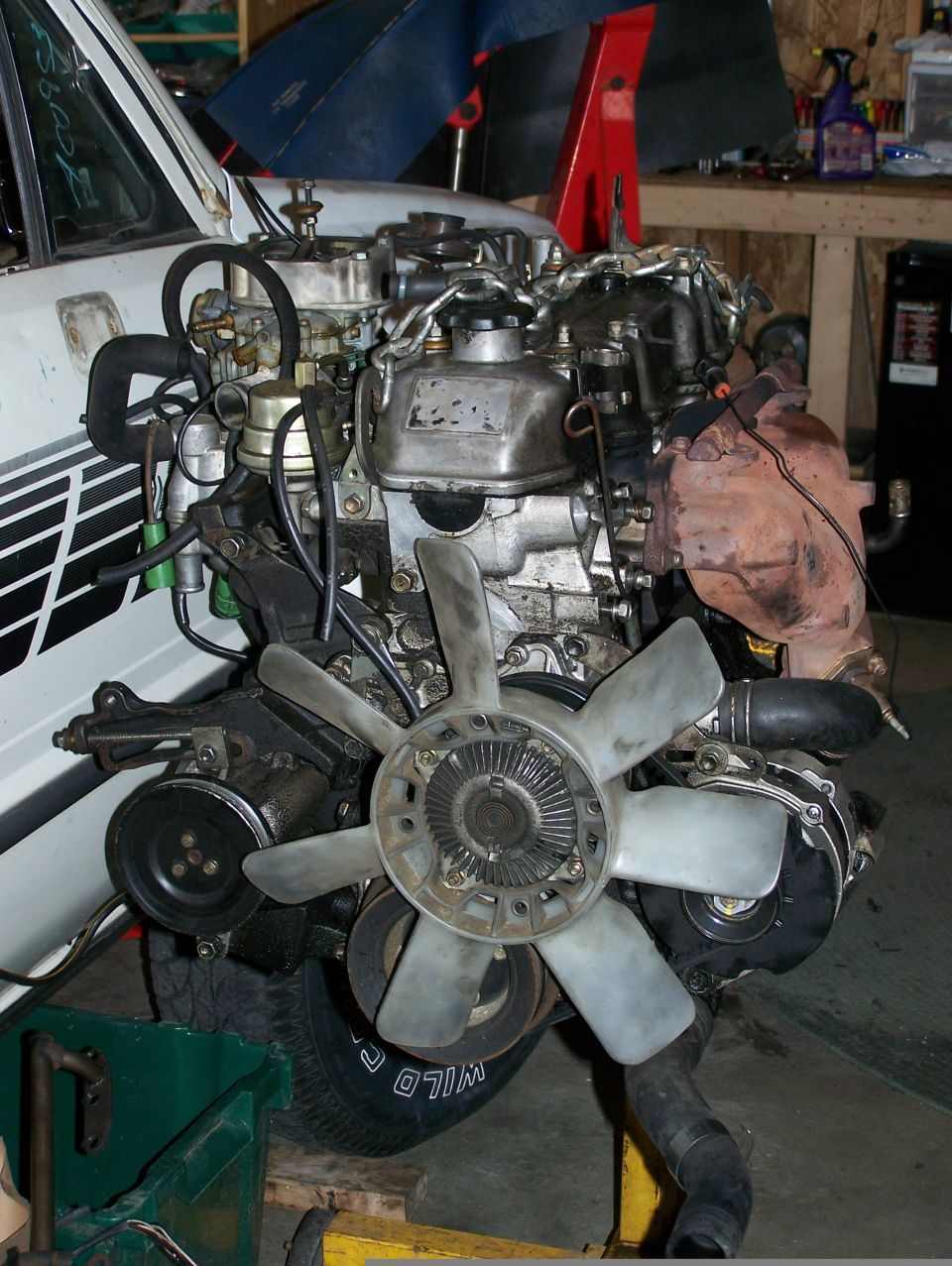 Engine assembly with fan, belts, and hoses, partially installed in a white vehicle