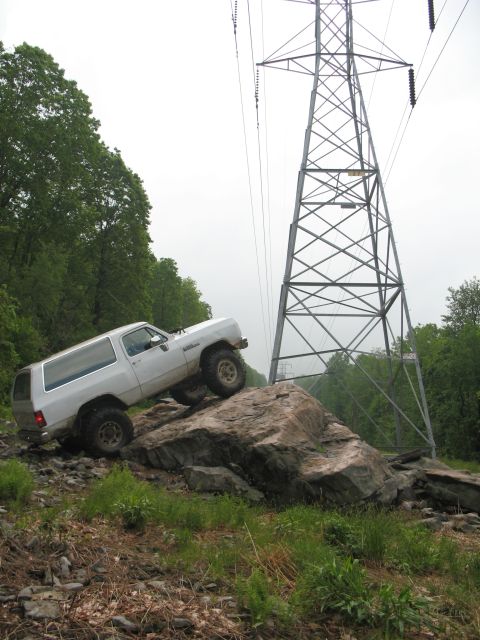 1985 Ford Bronco - This SUV is navigating a challenging rocky terrain near a tall power line tower.