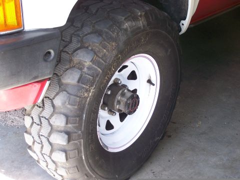 1988 Suzuki Samurai - Detail of a white wheel with a "TOYOTA" center cap, part of a red and white vehicle's front fender and tire.