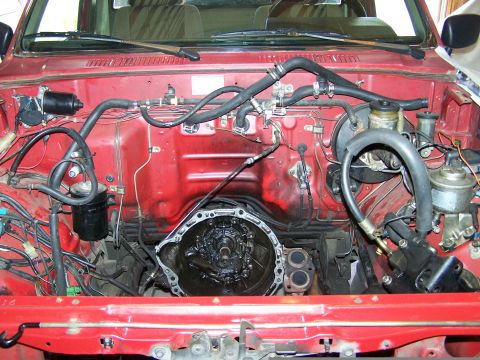 1988 Suzuki Samurai - The engine bay of a red pickup truck shows the transmission removed, revealing the engine block and surrounding components.