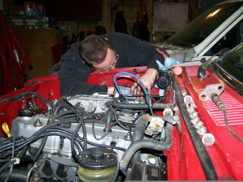 1988 Suzuki Samurai - Mechanic works on the engine of a red vehicle in a garage setting.