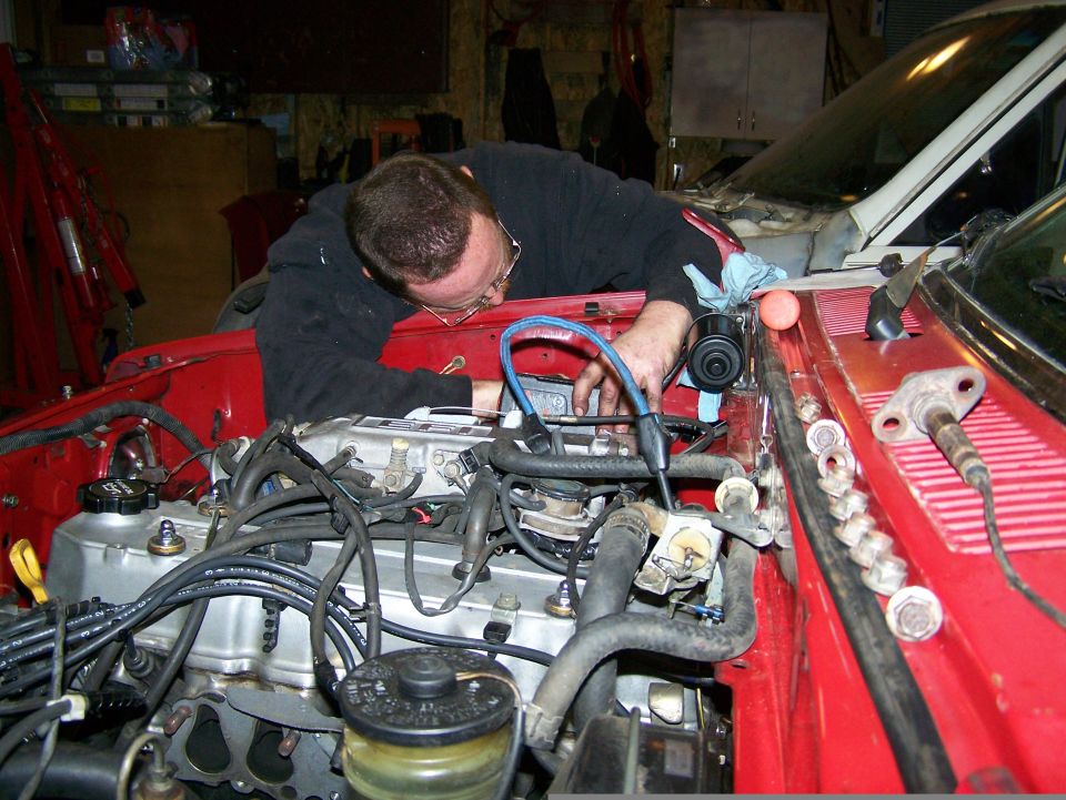 Red engine bay with a person working on the engine. Wires and hoses are visible