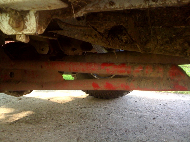 Underside of a vehicle frame with red painted components and a tire visible
