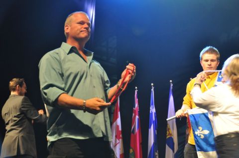 1996 Ford Bronco - A man on stage holds a red ribbon while several provincial flags are displayed in the background.