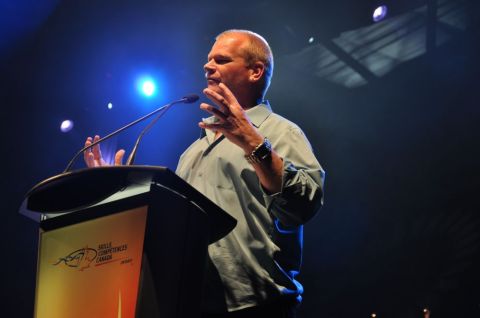 1996 Ford Bronco - Mike Holmes addresses an audience from behind a podium the 'Skills Competences Canada' logo.