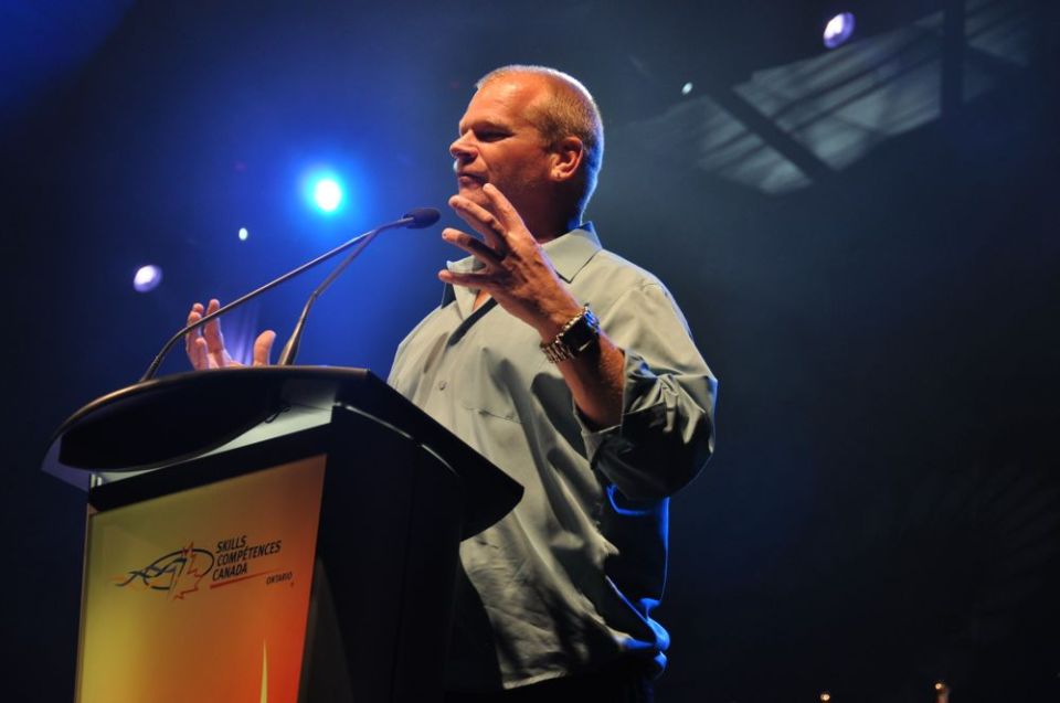 Mike Holmes speaking at a podium with 'Skills Competences Canada' logo