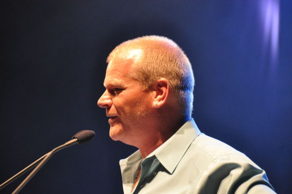 man with short hair and earring speaks into a microphone