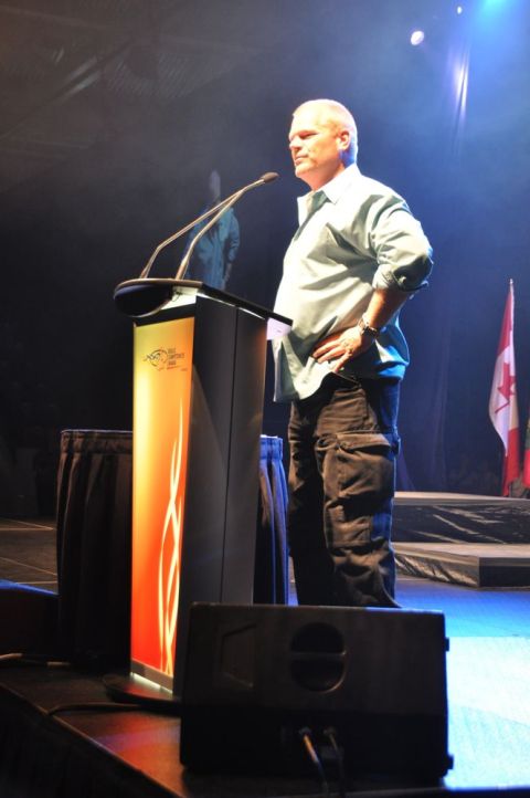 1996 Ford Bronco - A man speaks at a podium on a stage with a Canadian flag in the background.