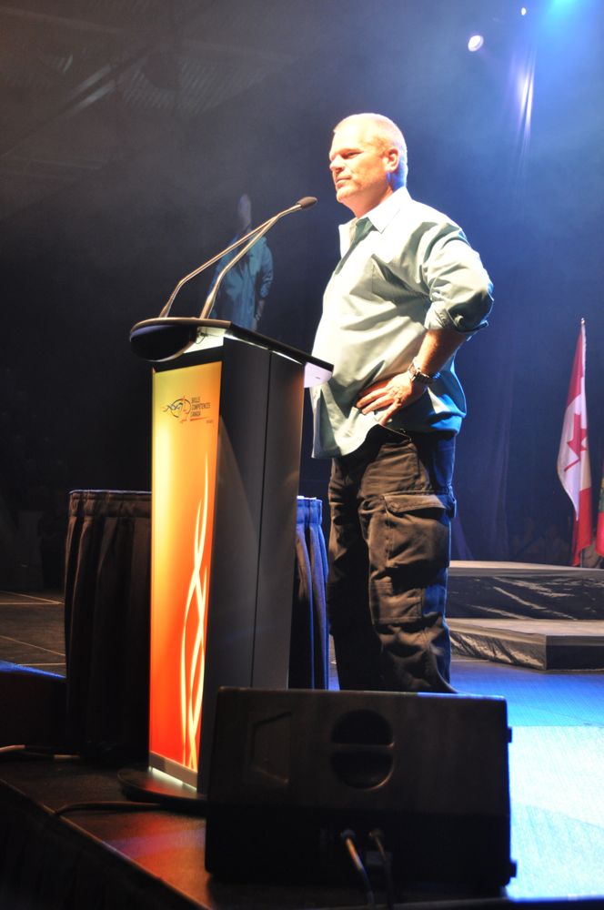 Man in light blue shirt and cargo pants stands at a podium with hands on hips