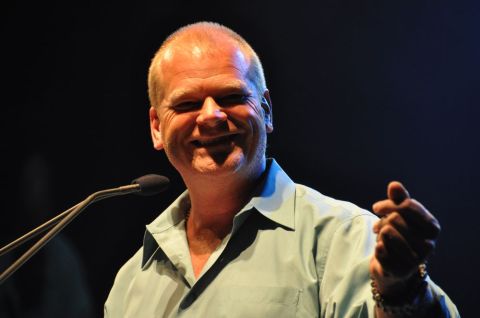 1996 Ford Bronco - A man in a light blue shirt smiles while speaking at a podium with a microphone.