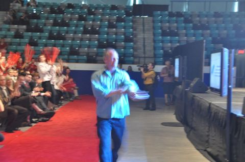 1996 Ford Bronco - A man walks down a red carpet in an arena, with an audience seated in the background and a stage to the right.
