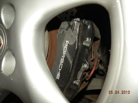 2000 Porsche Carrera - A close-up view of a Porsche branded brake caliper and rotor, partially obscured by a silver wheel.