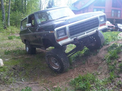 1979 Ford Bronco - This lifted black Ford Bronco is shown off-roading on a dirt path near a wooded area.