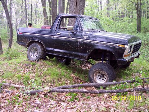 1979 Ford Bronco - This black 1979 Ford Bronco is shown navigating rough terrain in a forest setting.