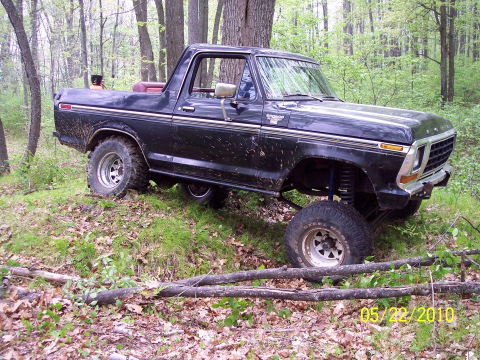 Black 1979 Ford Bronco with lifted suspension off-roading in a wooded area