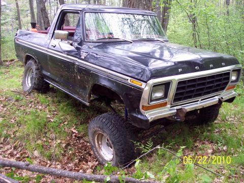 1979 Ford Bronco - This Ford Bronco is parked off-road in a wooded area, showing its lifted suspension and large tires.