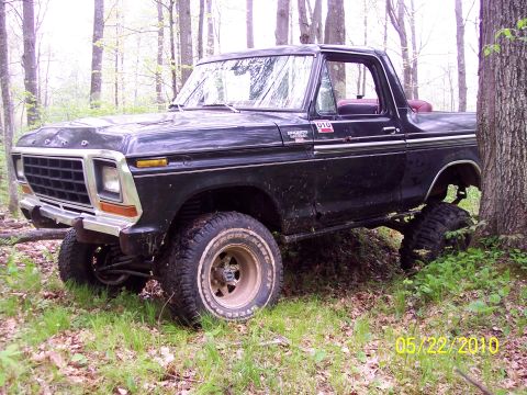 1979 Ford Bronco - A black 1978 Ford Bronco sits off-road in a forest with its front end angled towards the camera.
