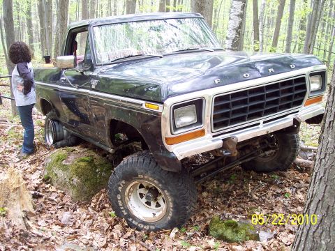1979 Ford Bronco - A black 1979 Ford F-Series truck is stuck on a large rock in a wooded area.