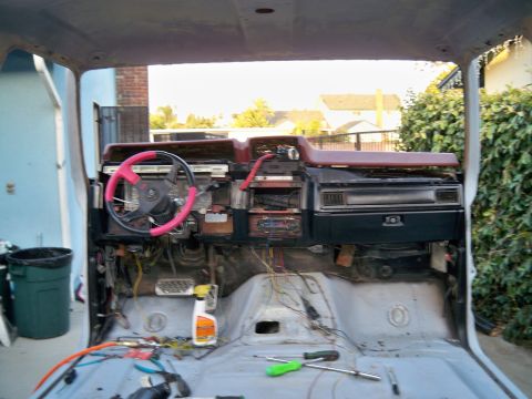 1985 Ford Bronco - The interior of a vehicle is shown with the dashboard disassembled, revealing exposed wiring and tools scattered on the floor.
