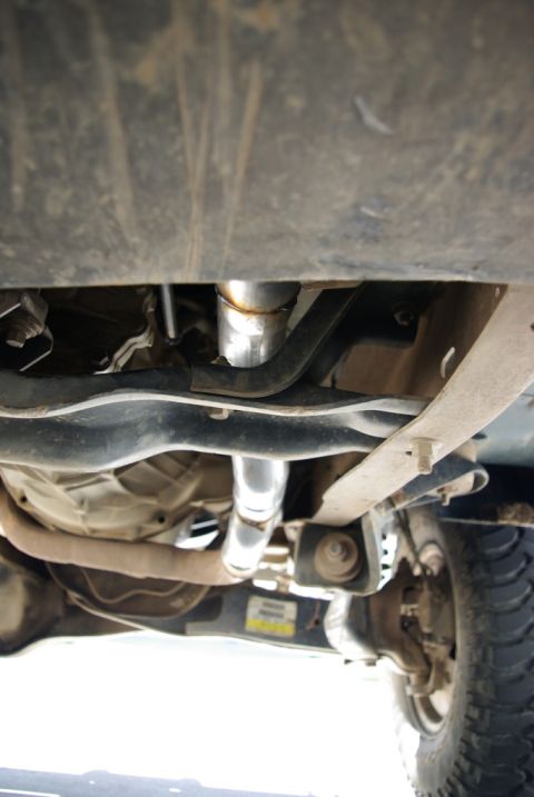 1995 Ford Bronco - View of the underbody exhaust system, showing shiny pipes and a leaf spring, with a partial view of the rear tire.